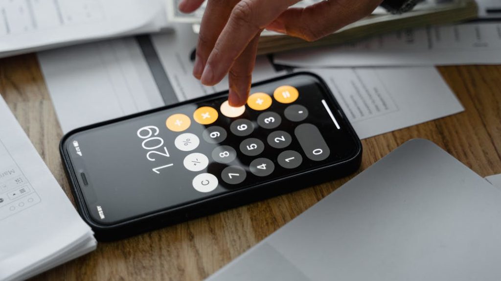 Close-up of a person using a smartphone calculator on a table with documents for financial calculations.